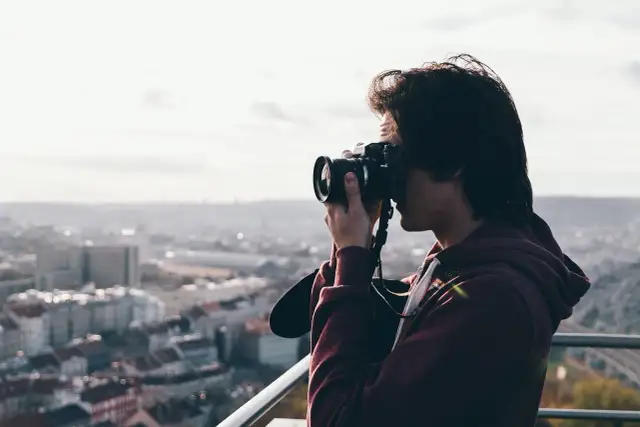 Przeswietlone zdjecie. Młody mężczyzna z aparatem fotograficznym w rękach, robiący zdjęcie miasta z góry.