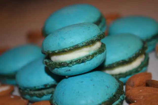 Stos niebieskich makaroników z białym kremem, otoczony migdałami.