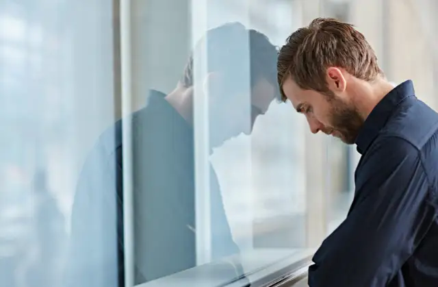 Mężczyzna opiera czoło o szybę, jego odbicie jest widoczne.