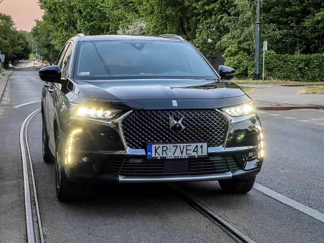 Czarny DS 7 z włączonymi światłami dziennymi stoi na torach tramwajowych.