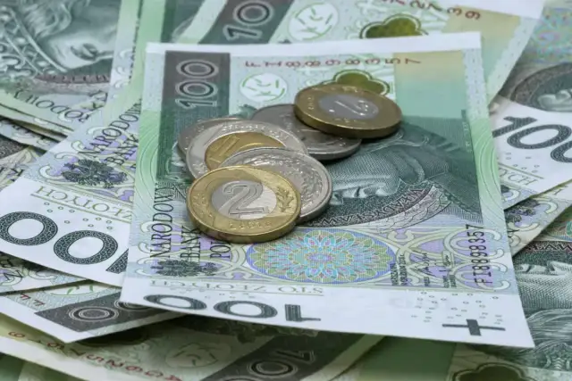 Stos polskich banknotów 100 zł i monet, w tym 2 zł.