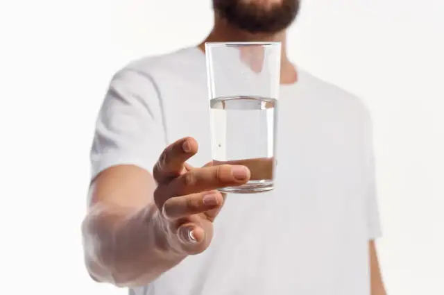 Mężczyzna trzyma szklankę z wodą. Zastanawiasz się, gdzie zbadać wodę z kranu?