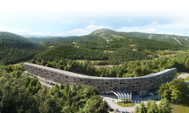 Nowoczesny, zakrzywiony budynek hotelu Mercure Szczyrk Resort otoczony lasem i górami.