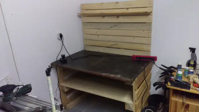 Drewniany stół warsztatowy z półkami, narzędziami i listwą zasilającą.