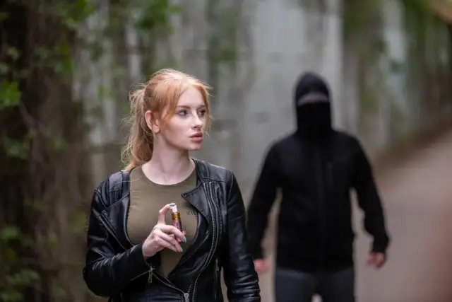 Kobieta z gazem pieprzowym w dłoni, w tle mężczyzna w kapturze.