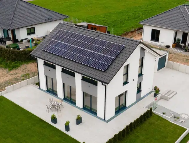 Nowoczesny biały dom z panelami słonecznymi na dachu, tarasem i ogrodem.