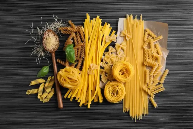 Różne rodzaje makaronu: spaghetti, fusilli, kokardki, tagliatelle, penne, nitki, na drewnianej łyżce.