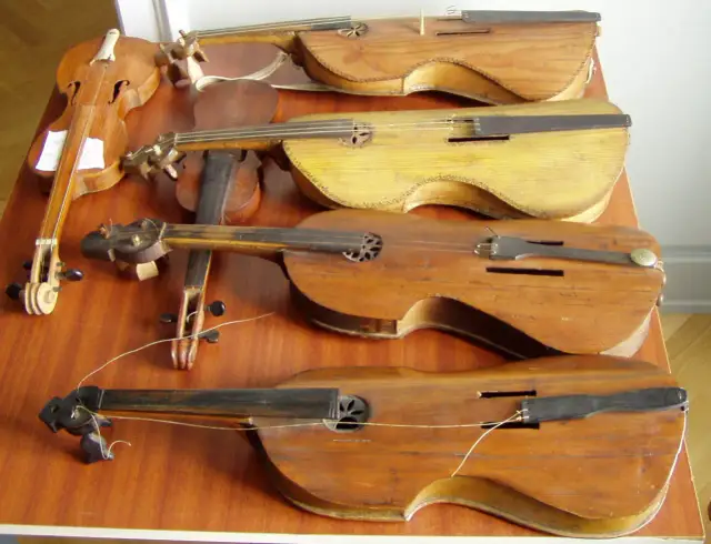 Kilka drewnianych instrumentów smyczkowych, w tym skrzypce, leżących na drewnianym stole.