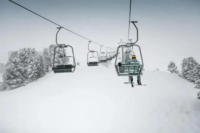 Osoba na nartach jedzie w górę stoku na krzesełkowym rodzaju wyciągu narciarskiego.