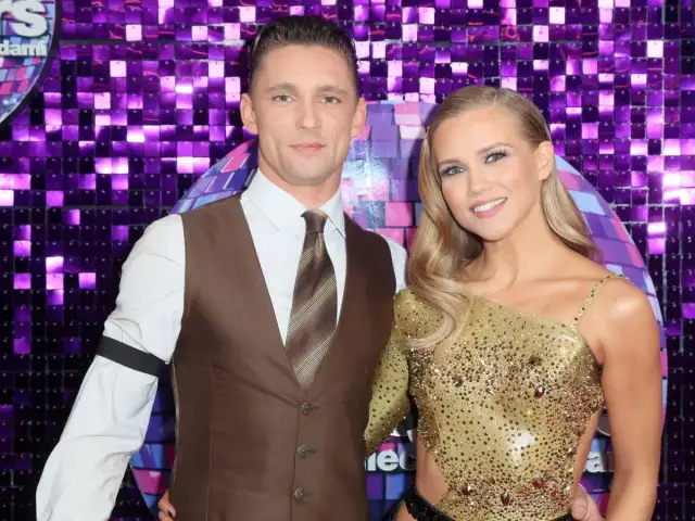 Kaczorowska i jej partner gotowi na Taniec z Gwiazdami. Ona w złotej, błyszczącej kreacji, on w eleganckim brązowym wdzianku.