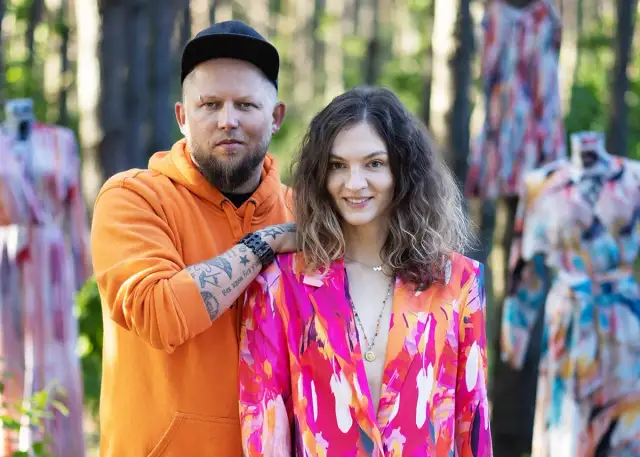 Para pozuje wśród kolorowych sukienek. Mężczyzna w pomarańczowej bluzie, kobieta w marynarce. Naoko - co to za firma?