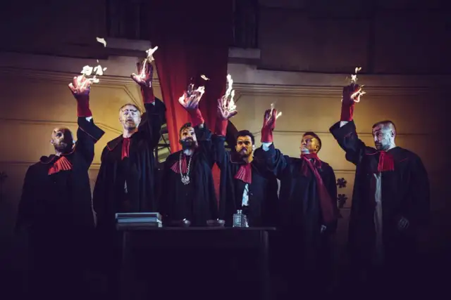 Mężczyźni w togach z płonącymi dłońmi, jakby odtwarzali legendę o czarciej łapie.