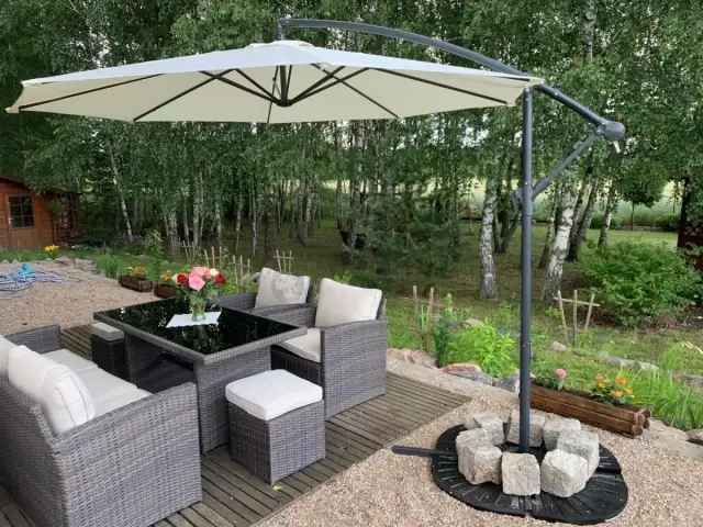Parasol ogrodowy z kamiennym obciążeniem podstawy, meble rattanowe i stół w ogrodzie.