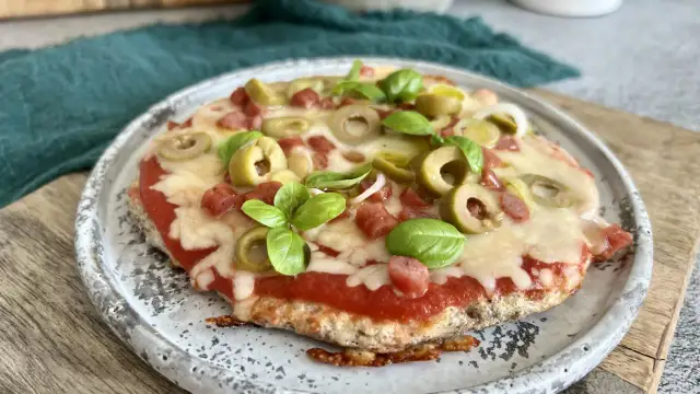 Mini pizza z serka wiejskiego, z sosem pomidorowym, oliwkami, kiełbaską i bazylią, na talerzu.