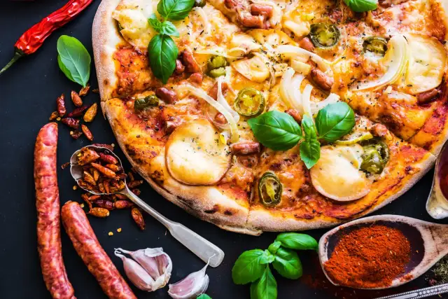 Apetyczna pizza z kiełbasą, cebulą i papryczkami jalapeño, otoczona składnikami.