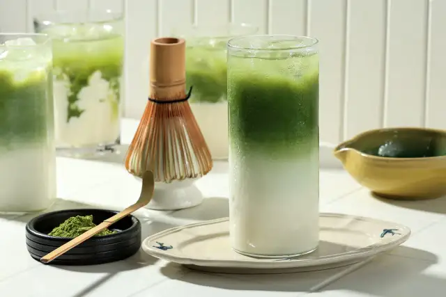 Orzeźwiające matcha latte z lodem, obok bambusowa miotełka i proszek matcha. Idealne na co dzień.