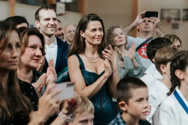 Agnieszka Grochowska z uśmiechem klaszcze, otoczona ludźmi na widowni.