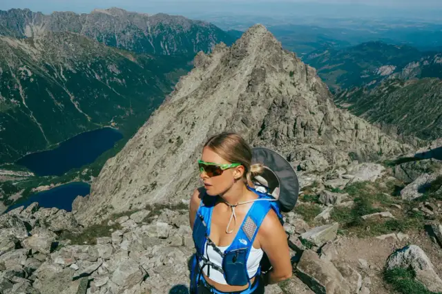 Kobieta w okularach i niebieskim plecaku na tle skalistych gór w Polsce. Widok na jeziora i szczyty.