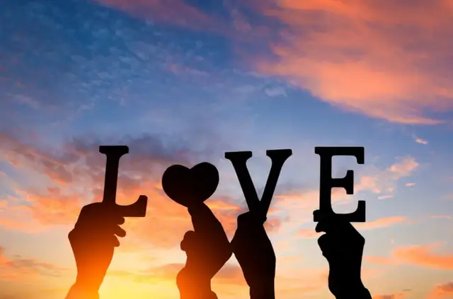 Dłoń trzyma serce, tworząc napis LOVE na tle zachodzącego słońca. To dzień najbardziej kochanych.