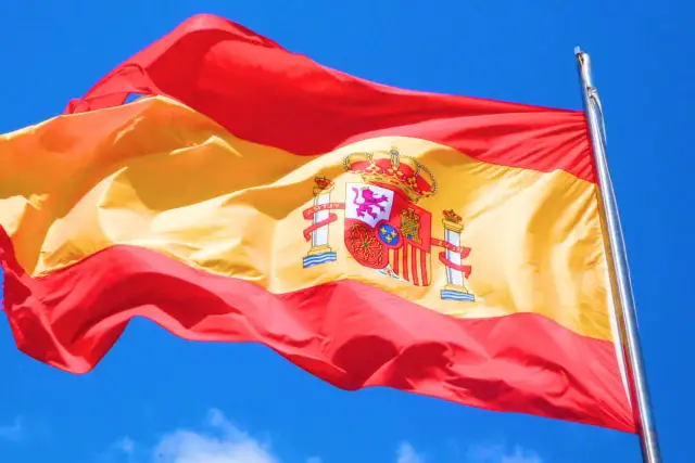 Flaga Hiszpanii powiewa na wietrze na tle błękitnego nieba.