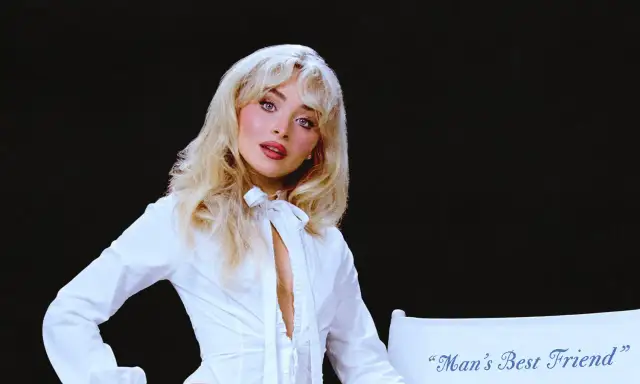 Sabrina Carpenter w białej koszuli, z rozpuszczonymi blond włosami, wygląda jak "man's best friend" na tle czerni.
