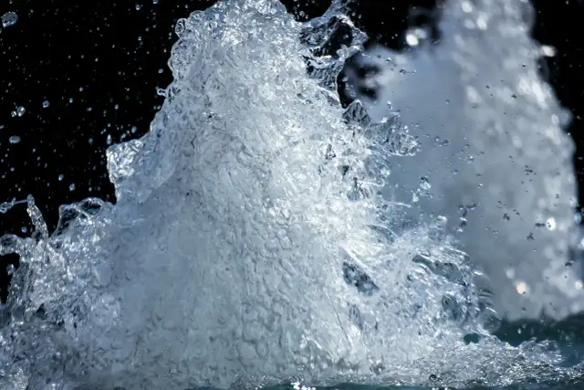 Rozpryskująca się woda z kranu na czarnym tle.