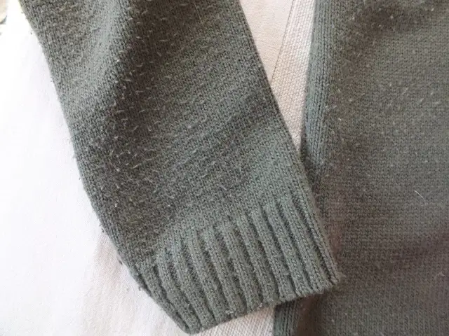 Zielony sweter z dzianiny, na którym widać mechacenie. Czy wiskoza się mechaci? Tak, ten materiał pokazuje oznaki zużycia.