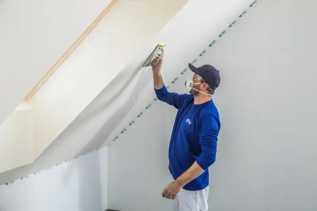Budowlaniec szlifuje ścianę pod skosem, wyjaśniając, dlaczego gips szpachlowy szybko twardnieje.