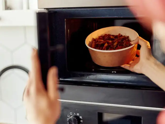 Ręka wkłada miskę z jedzeniem do mikrofalówki. Tak działa mikrofalówka: podgrzewa jedzenie za pomocą fal.