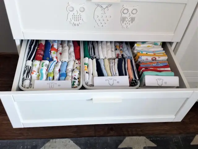 Ubranka dla noworodka schludnie ułożone w szufladzie. Widać kolorowe pajacyki, body i śpioszki, posegregowane według rozmiaru.