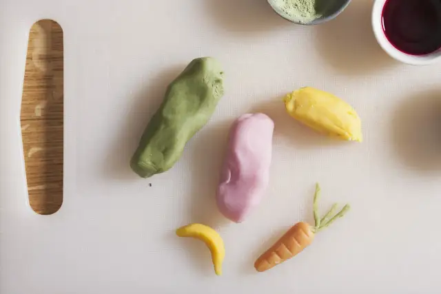 Kolorowe masy cukrowe uformowane w marchewkę, banana i inne kształty na białej desce.