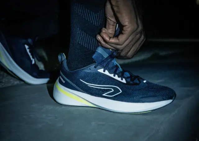 Dłoń sznuruje granatowe buty do biegania z żółtym akcentem.