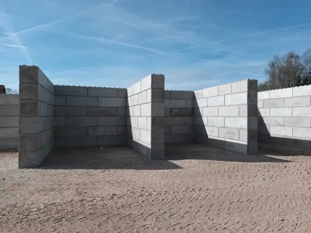 Budowa muru oporowego z bloczków betonowych. Zbrojenie widoczne na górze ścian.