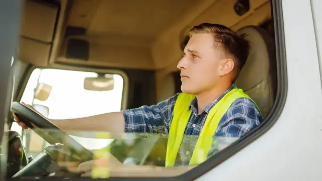 Młody kierowca w kamizelce odblaskowej za kierownicą ciężarówki.