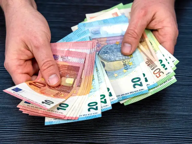 Dłonie trzymają plik banknotów euro, które są walutą w Hiszpanii. Widoczne nominały to 10, 20 i 50 euro.