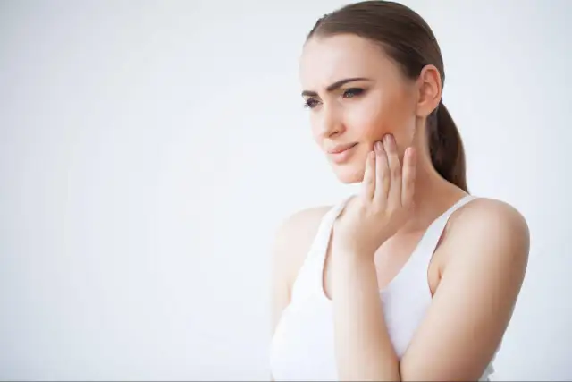 Kobieta z ręką na policzku, odczuwająca ból.