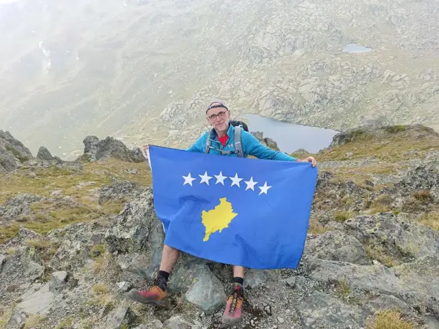 Mężczyzna z flagą Kosowa na szczycie góry. Niesamowite kosowo wakacje w górach.
