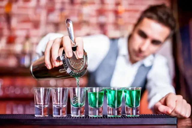 Barman nalewa zielony alkohol do kieliszków na barze.