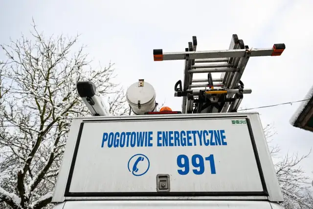 Tył białego samochodu pogotowia energetycznego z napisem "POGOTOWIE ENERGETYCZNE 991" i drabiną na dachu.