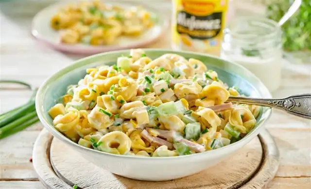 Sałatka z tortellini, szynką, kukurydzą i ogórkiem w sosie majonezowym, posypana szczypiorkiem.