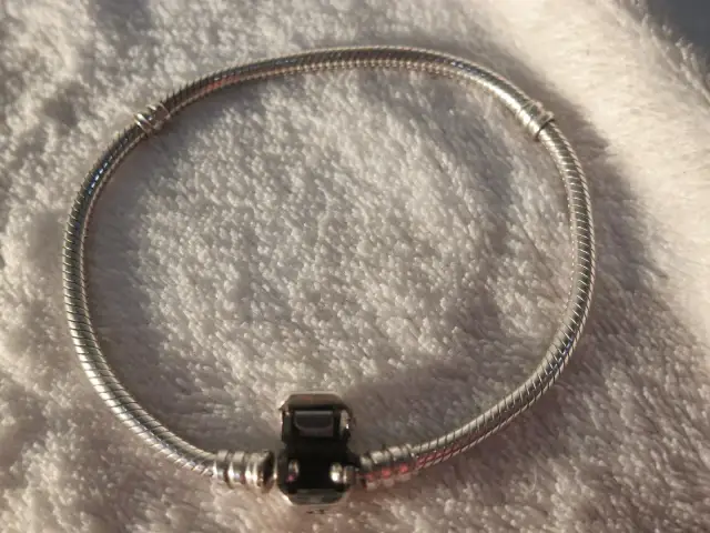 Srebrna bransoletka Pandora z zapięciem na tle białego materiału.