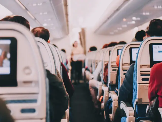 View from inside an airplane cabin, showing rows of seats with passengers and entertainment screens.