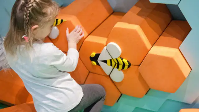 Dziewczynka dotyka dekoracji w kształcie plastra miodu z pszczołami.