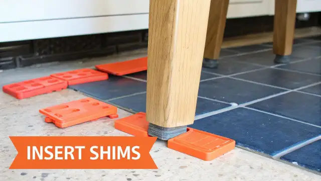 Pomarańczowe kliny pod nogą mebla pomagają jak wypoziomować szafę na krzywej podłodze.