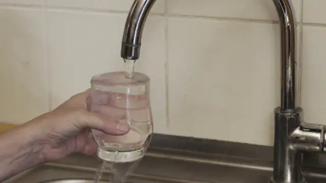 Ręka trzyma szklankę pod strumieniem wody z kranu.