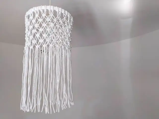 Oto jak zrobić abażur ze sznurka jutowego: ręcznie robiony, biały, makramowy klosz z frędzlami, wiszący na suficie.