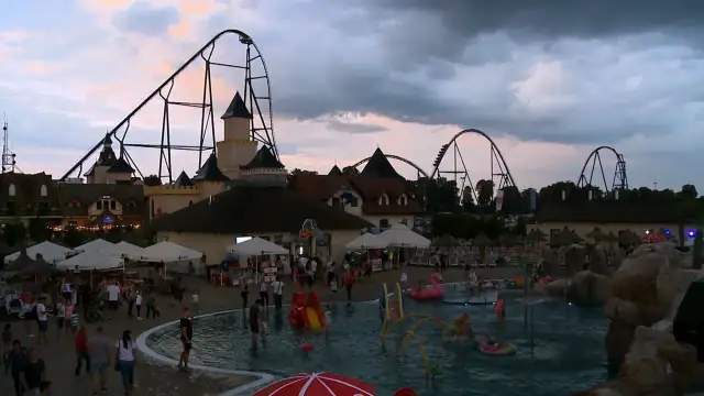 Park rozrywki z kolejką górską i basenem, ludzie odpoczywają.