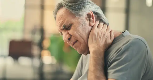 Starszy mężczyzna zamyka oczy, trzymając się za kark. Może to być jeden z objawów zapalenia opon mózgowych.