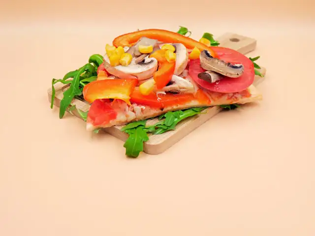 Kawałek pizzy wegetariańskiej z pomidorem, papryką, pieczarkami i kukurydzą na desce.