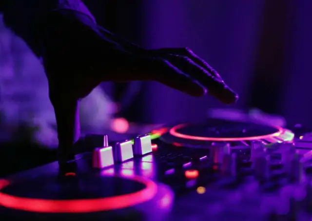 Dłoń DJ-a nad konsolą z czerwonymi i fioletowymi światłami.